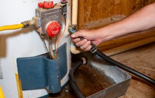 Plumber connecting hose to drain water heater during maintenance service in Highlands Ranch Colorado